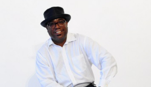 Michael Valentine, host of 88 Jazz Place and Classics & Grooves on WDNA 88.9FM, smiling in a stylish black hat and white shirt.